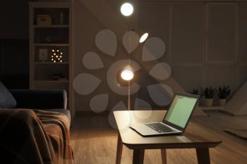 Modern laptop on table in interior of living room at night�