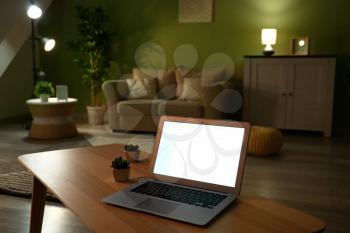Modern laptop on table in living room at night�