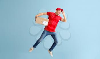 Jumping young male courier with box on grey background�