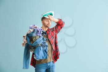Stressed young man with iron and clothes on grey background�