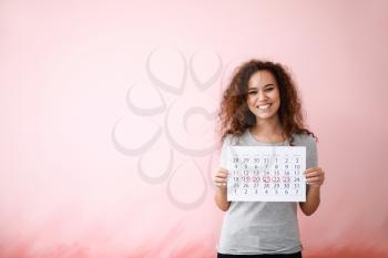 African-American woman holding calendar with marked days of menstruation on color background�