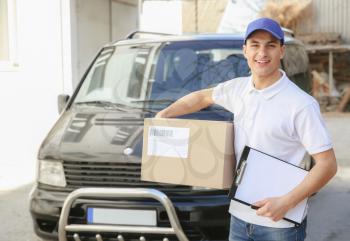 Delivery man with parcel and clipboard near car outdoors�