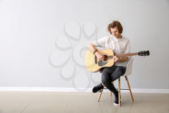 Handsome young man playing guitar near light wall�