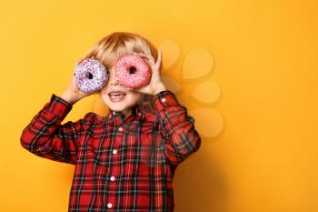 Happy little boy with tasty donuts on color background�