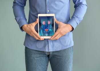 Man holding tablet computer with urinary system on screen against grey background�