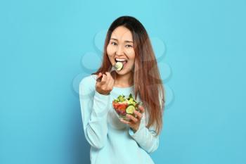 Asian woman with vegetable salad on color background�