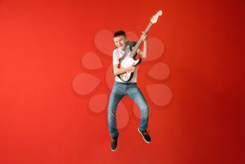 Teenage boy playing guitar against color wall�