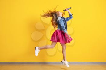 Teenage girl with microphone jumping and singing against color wall�