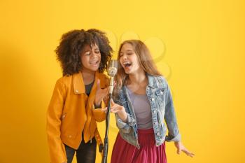 Teenage girls with microphone singing against color background�