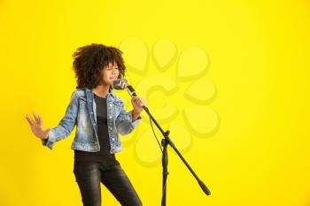 African-American girl with microphone singing against color background�