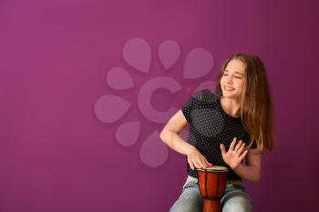 Teenage girl playing drum against color background�