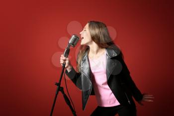 Teenage girl with microphone singing against color background�