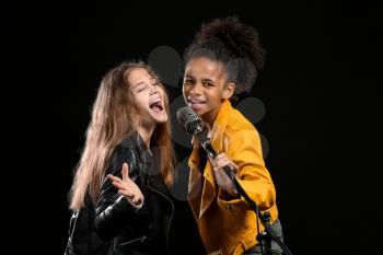 Teenage girls with microphone singing against dark background�