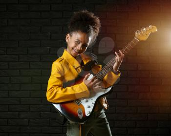 African-American girl playing guitar against dark wall�