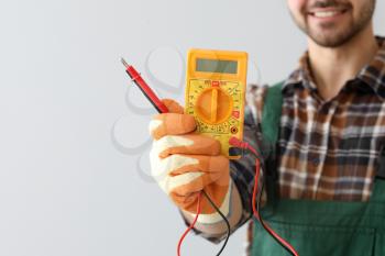 Male electrician with multimeter on light background�