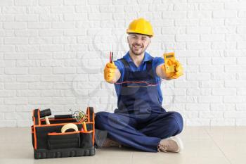 Male electrician with tools kit sitting near white brick wall�