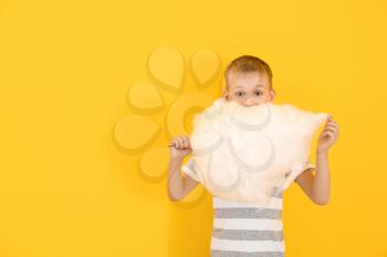 Cute little boy with cotton candy on color background�
