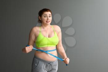 Overweight woman with measuring tape on grey background. Weight loss concept�