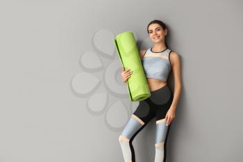 Sporty woman with yoga mat on grey background�