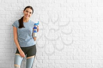 Sporty woman with bottle of water near brick wall�