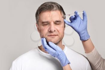 Mature man and hands holding syringe for anti-aging injections on grey background�