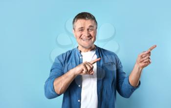 Handsome mature man pointing at something on color background�