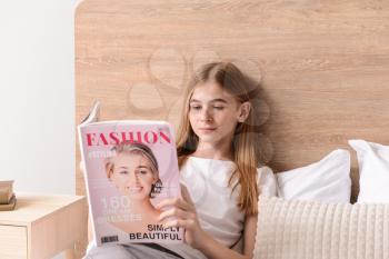 Cute teenage girl reading fashion magazine in bedroom at home�