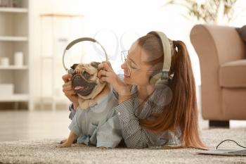 Teenage girl with cute pug dog listening to music at home�