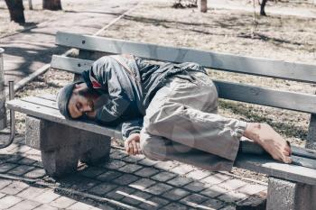 Poor homeless man lying on bench outdoors�