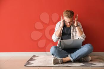 Stressed young man with laptop sitting near color wall�
