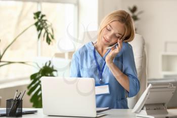 Female medical assistant talking by phone while working on laptop in clinic�