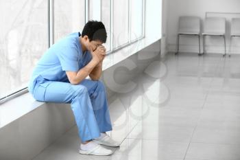Depressed male medical assistant sitting on window sill in clinic�