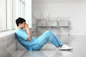 Depressed male medical assistant sitting near window in clinic�