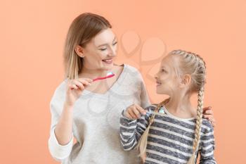 Little girl and her mother cleaning teeth on color background�