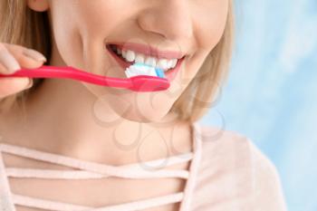 Beautiful woman cleaning teeth on light background, closeup�