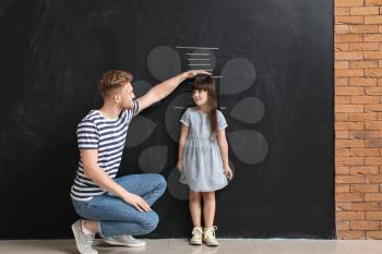 Father measuring height of his little daughter near wall with marks�