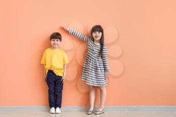 Cute little children measuring height near color wall�