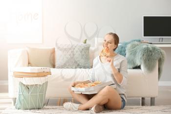 Beautiful woman eating tasty pizza at home�