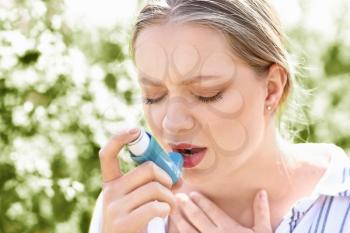 Woman with inhaler having asthma attack outdoors�