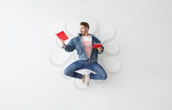 Jumping young man with books on light background�
