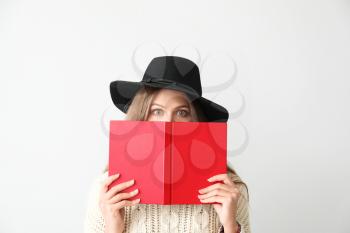 Shocked young woman with book on light background�
