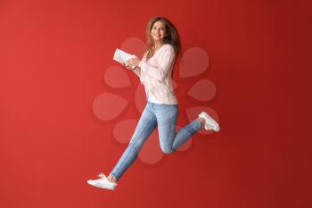 Jumping young woman with books on color background�