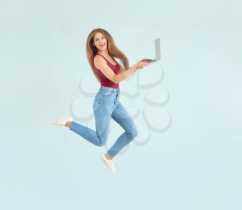 Beautiful jumping woman with laptop on color background�