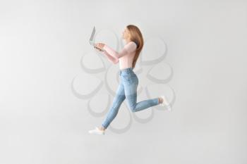 Jumping young woman with laptop on light background�