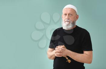 Senior Muslim man praying against color background�