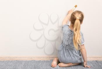 Little girl painting on light wall�