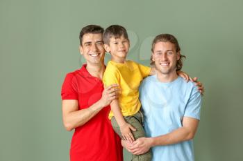 Happy gay couple with adopted child on color background�