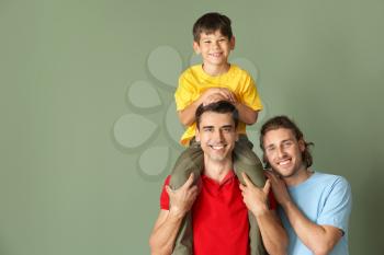 Happy gay couple with adopted child on color background�