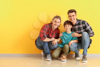 Happy gay couple with adopted child near color wall�