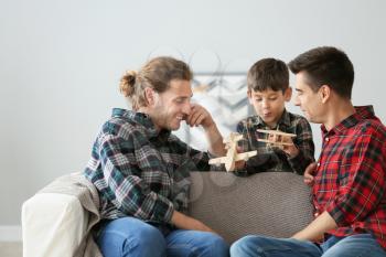 Happy gay couple playing with adopted child at home�